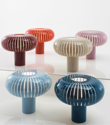 Sei lampade da tavolo decorative di Kartell, in diversi colori, con un design a forma di fungo su una superficie riflettente.