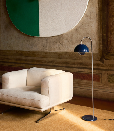 Elegante lampada da terra &Tradition accanto a una moderna poltrona lounge in un ambiente caldo.