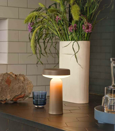 Lampada da tavolo portatile Muuto su un piano cucina scuro con decorazioni floreali.