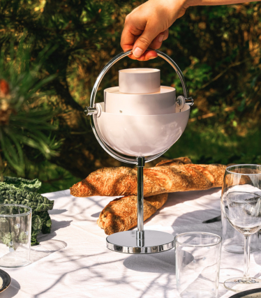 Lampada da tavolo portatile GUBI su un elegante tavolo da giardino al sole.