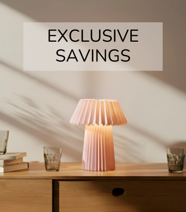 Lampada da tavolo rosa pallido su una credenza in legno, circondata da bicchieri e libri alla calda luce del sole.