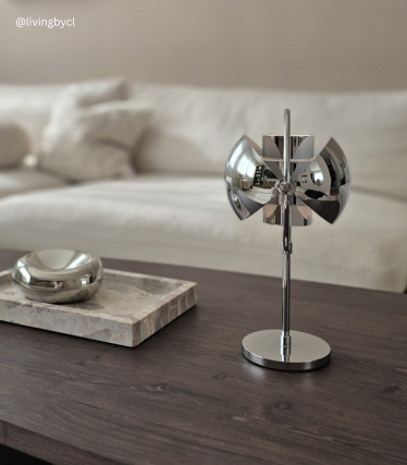 Lampada da tavolo di design cromata su un tavolo in legno, davanti a un divano chiaro.