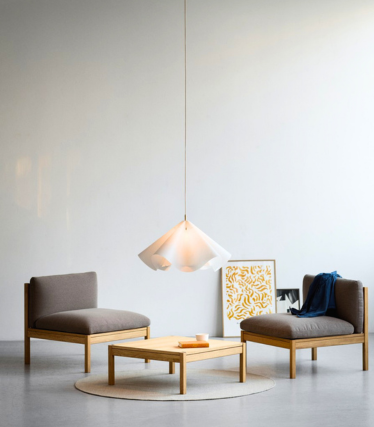 Lampada a sospensione leggera sopra poltrone basse, in un ambiente calmo e minimalista.