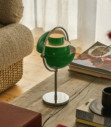 Lampada da tavolo Multi-Lite verde con base cromata su un tavolo in legno accanto a dei libri.