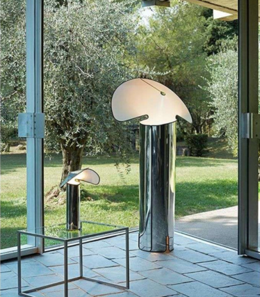 Due lampade da terra lucide con paralumi curvi a forma di foglia davanti a una finestra con vista sul giardino.